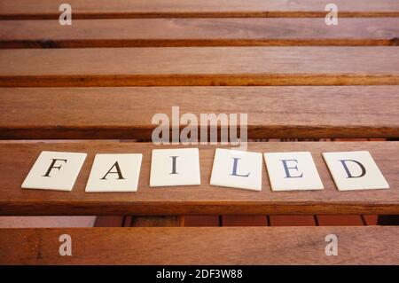 Das Wort scheiterte geschrieben durch Buchstaben auf kleinen Quadraten auf Eine Holzbank unter den Lichtern Stockfoto