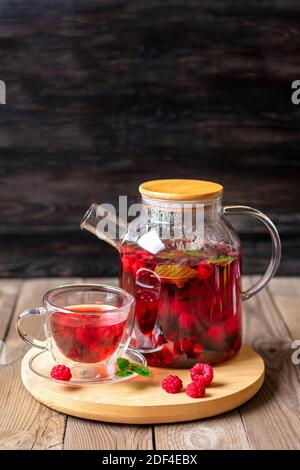 Kräutertee mit Beeren, Himbeeren, Minzblättern und Hibiskusblüten in Glas Teekanne und Tasse auf Holztisch Medizin für kaltes Vitamin Drink Rustikal Stockfoto