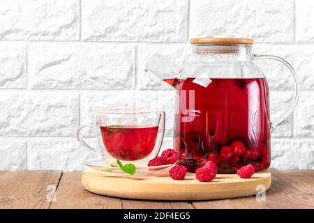 Kräutertee mit Beeren, Himbeeren, Minzblättern und Hibiskusblüten in Glas Teekanne und Tasse auf Holztisch Medizin für kaltes Vitamin Drink Rustikal Stockfoto