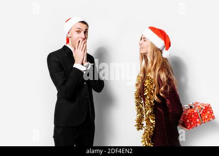 Ein glückliches Paar von Liebenden, in Santa Claus Hüte, das Mädchen gibt dem Kerl ein Weihnachtsgeschenk. Auf weißem Hintergrund. Stockfoto