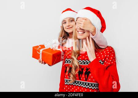 Tochter mit Mutter in Weihnachtsmützen und Weihnachtspullover, Tochter gibt ein Weihnachtsgeschenk an Mutter, auf weißem Hintergrund. Stockfoto