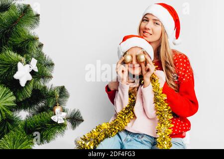 Mama und Tochter tragen Weihnachtsmann Hüte, in Silvester Pullover, feiern das neue Jahr durch das Spielen mit Weihnachtskugeln. Auf weißem Hintergrund. Stockfoto