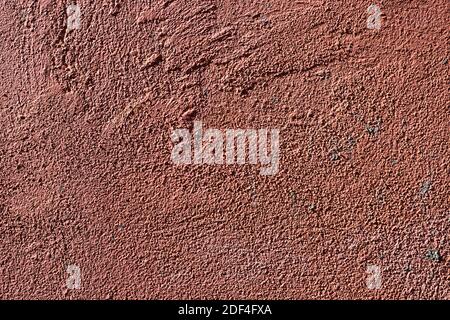 Rustikaler Putz an der verzweifelten Wand. Konkrete Fototextur. Orangefarbene rote Textur. Grungy Korn bemalte Wand in Sonnenlicht. Nahaufnahme aus rauem Beton für Retro Stockfoto