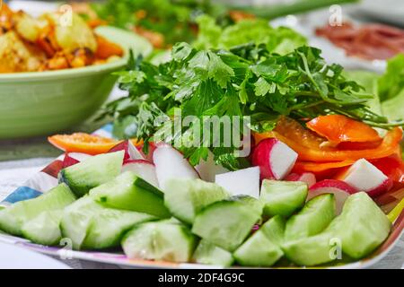 Salat aus Gurken, Tomaten, Radieschen und Kräutern auf einem Teller auf einem gedeckten Tisch. Gesunde Ernährung Stockfoto