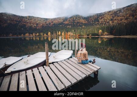 Reisende Mädchen mit Entspannung durch Herbst nebligen See bei Sonnenaufgang. Junge Frau sitzt auf Pier bewundern die wunderbare Landschaft.Wanderlust, Lifestyle-Konzept Stockfoto