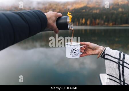 Reisender Mann Gießen ein heißes Getränk aus Thermoskanne zu Tasse. Junge Frau trinkt heißes Getränk bei Tasse. Herbstsaison.Outdoor-Paar, Reisekonzept. Stockfoto