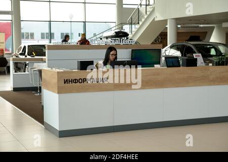 Ein Mädchen sitzt an der Rezeption, mit einer Inschrift in russischer Information, in der Halle eines Autohauses vor dem Hintergrund eines Fensters. Stockfoto