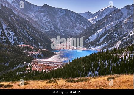 Türkisfarbener See zwischen schneebedeckten Bergen an sonnigen Tagen in der Wintersaison; großer Almaty See in Kasachstan Stockfoto