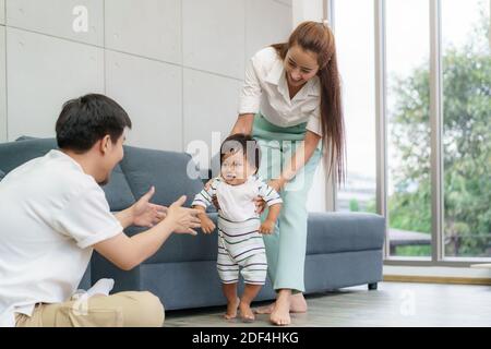 Asiatische Sohn Baby nimmt erste Schritte gehen nach vorne zu seinem Vater. Happy Little Baby lernen, mit Mutter Hilfe zu gehen und zu lehren, wie man sanft ho zu gehen Stockfoto