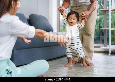 Asiatische Sohn Baby nimmt erste Schritte gehen nach vorne zu seiner Mutter. Happy Little Baby lernen, mit Vater Hilfe zu gehen und zu lehren, wie man sanft ho zu gehen Stockfoto