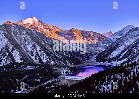 Majestätischer Berggipfel steigt über dem See in den letzten Strahlen der untergehenden Sonne; Hochland in der Wintersaison bei Sonnenuntergang Stockfoto