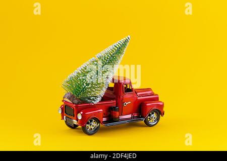 Roter Retro Spielzeug LKW mit Weihnachtsbaum auf LKW-Körper auf gelbem Hintergrund. Lieferung, weihnachten, Neujahrskonzept. Vintage Spielzeug Modell Auto mit Christm Stockfoto