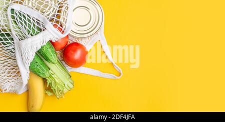 Lieferung von Lebensmitteln. Lebensmittel in einem Saitenbeutel auf gelbem Hintergrund. Konserven, Tomaten, Gurken, Bananen. Spende, Coronavirus. Lebensmittel für Stockfoto