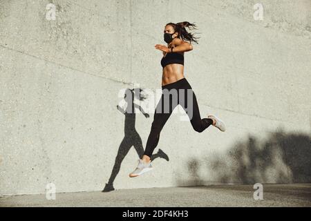 Athletische Frau mit Gesichtsmaske läuft im Freien. Weibliche Läuferin in Sportkleidung und Schutzmaske sprintet im Freien. Stockfoto