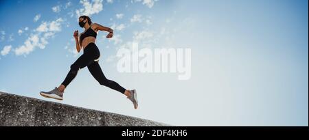 Low-Angle-Aufnahme einer Sportlerin, die über eine Wand gegen den blauen Himmel läuft. Panorama-Aufnahme einer Frau in Sportbekleidung und schützende Gesicht ma Stockfoto