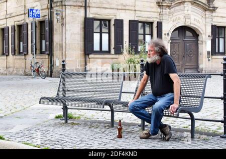 Mann sitzt (sitzend) auf einer Bank, trinkt und raucht im Stadtzentrum. Stockfoto