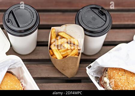 Fast Food. Pappbecher mit Kaffee, Hamburger-Boxen und Pommes auf einer Parkbank.Takeaway Food-Konzept. Stockfoto