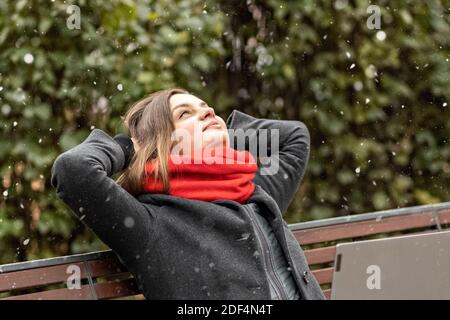 Eine junge Frau, mit den Händen hinter dem Kopf, fühlt Ruhe, ruht nach der Arbeit, sitzt auf einer Holzbank im Park ein Laptop auf den Knien. Pause während w Stockfoto