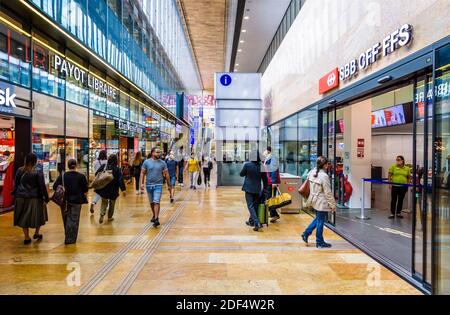 Die Fahrgäste laufen entlang der Querbahn im Genfer Bahnhof, vorbei an den Geschäften und dem SBB CFF FFS Informationsschalter. Stockfoto