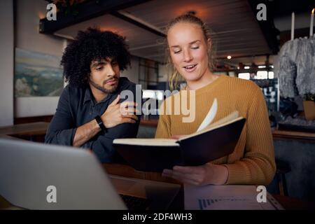 Junge männliche und weibliche Geschäftsleute, die sich Notizen in Tagebuch während der Arbeit mit Laptop in einem modernen Café Stockfoto