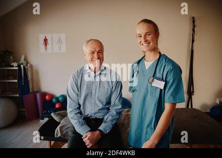 Porträt eines lächelnden älteren Mannes mit einem jungen Arzt in Uniform Und Stethoskop, das die Kamera betrachtet Stockfoto