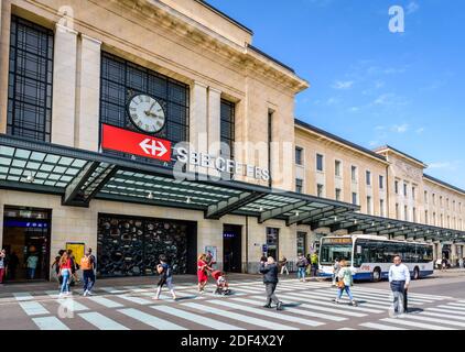 Die Menschen nehmen den Fußgängerübergang vor dem Haupteingang zum Bahnhof Genf-Cornavin, während ein Bus hält. Stockfoto