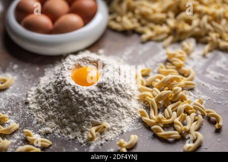 Mehlhaufen mit Eigelb und frischer Pasta auf einem Kochtisch. Stockfoto