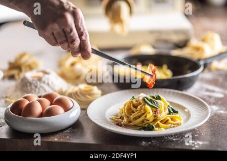 Fettuccine mit frischem Basilikum überzogen, indem man ein gebackenes Speckstück mit einer Pinzette darauf legt. Stockfoto