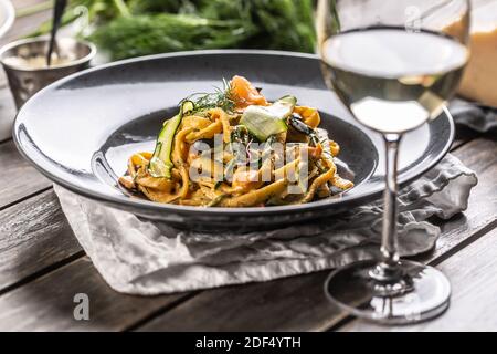 Lange Pasta mit geräuchertem Lachs und Zucchini auf einem dunklen Teller neben einem Glas Weißwein. Stockfoto