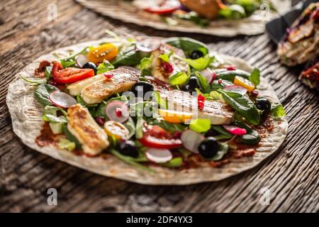 Offene vegetarische Tortilla mit Salat, Radish, chery Tomaten, Oliven, Granatapfel und gegrilltem Haloumi-Käse. Stockfoto