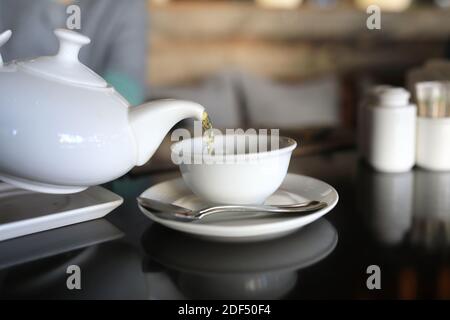 Person gießt Tee aus der weißen Teekanne im Restaurant Stockfoto