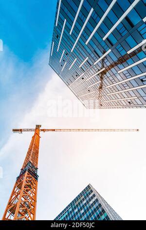 Gelber Turmdrehkran. Blick von unten auf einen hohen Baukran neben einem modernen Gebäude. Stockfoto