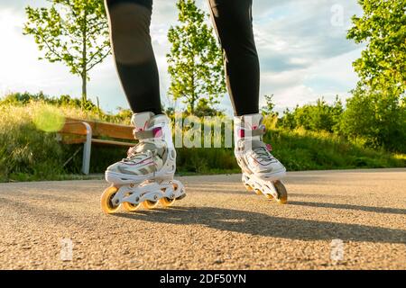 Frauenbeine mit Rollerklingen an sonnigen Tagen. Nahaufnahme der weißen Inline-Schlittschuhe auf dem Pfad. Stockfoto