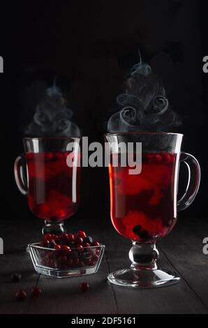 Weihnachtlicher roter Glühwein mit Beeren und Dampf als Weihnachtsbaumform in zwei transparenten Weingläsern auf schwarzem Holztisch im dunklen Innenraum, ver Stockfoto