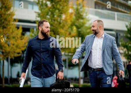 Zufriedene Kollegen auf dem Weg ins Büro diskutieren über das Projekt. Geschäftsleute, die draußen gehen, Papiere halten, reden, lachen. Stockfoto