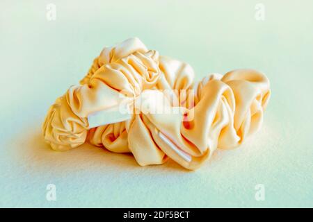 Gelbe Seide Scrunchyes auf grauem Hintergrund. Friseurwerkzeuge und Zubehör - Haarschrubben, elastische Haarbänder, Bobble Sport Scrunchie Haarband Stockfoto