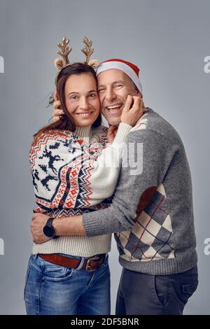 Ein glückliches Paar mittleren Alters lachte und umarmte sich gegenseitig mit einem weihnachtsmütze und ein Elchband Stockfoto