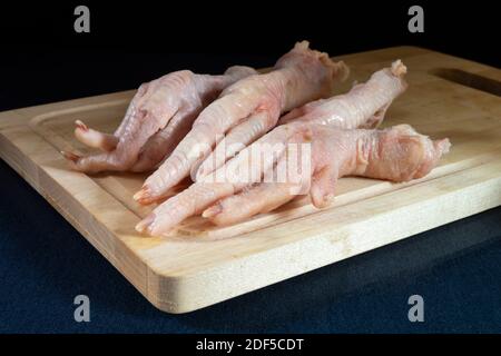Die Hühnerpfoten auf Holzbrett auf dem Tisch. Feuchte Produkte der Fütterung auf schwarzem Hintergrund Stockfoto