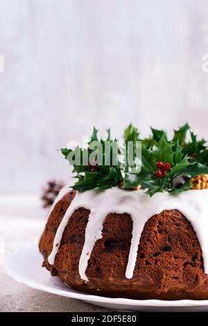 Weihnachten hausgemachte dunkle Schokolade gebündelt Kuchen mit weißer Glasur verziert Und Stechbeerzweige aus der Nähe Stockfoto