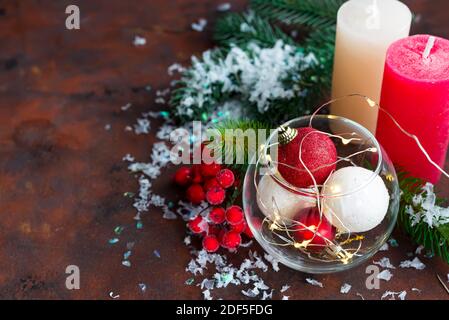 Rot-weiße Weihnachtskugel im Glas, Farbkerzen, Tannenzweigen und Beeren auf dunklem Steingrund mit Kopierraum Stockfoto