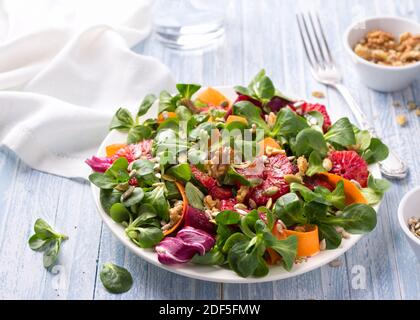 Grüner Salat mit Blutorangen, Karotten, Rüben, Samen und Nüssen auf hellblauem Hintergrund, freier Platz. Leckere gesunde Lebensmittel Stockfoto