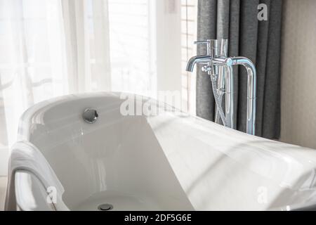 Moderne weiße Badewanne im geräumigen Badezimmer mit Glaswand. Elegantes Spa-Zimmer im Hotelresort. Sonniges weißes Badezimmer mit Chrom-Wasserhahn Stockfoto