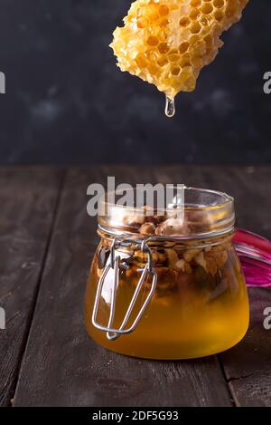 Honigkamm tropft aus dem Dipper in ein Glas mit Nüssen auf alten Holztisch. Gesunde Ernährung Stockfoto