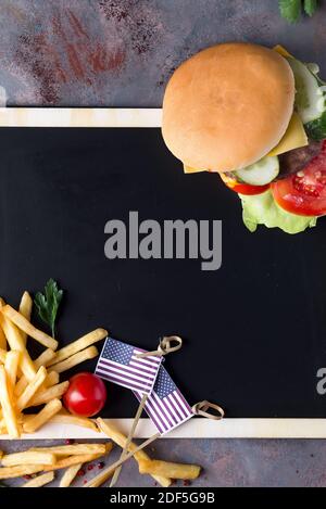 Leckere gegrillte hausgemachte Burger Kochen mit Rindfleisch, Tomaten, Käse, Gurke und Salat auf einer Kreidetafel mit Pommes Frites und der US-Flagge Stockfoto