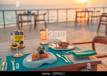 Tolles romantisches Abendessen am Strand auf der Holzterrasse mit Kerzen unter dem Sonnenuntergangshimmel. Romantik und Liebe, Luxus-Destination Dining, exotische Tisch-Setup Stockfoto