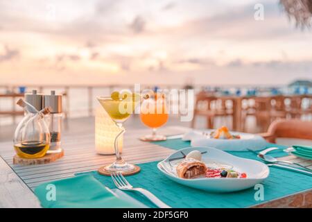 Tolles romantisches Abendessen am Strand auf der Holzterrasse mit Kerzen unter dem Sonnenuntergangshimmel. Romantik und Liebe, Luxus-Destination Dining, exotische Tisch-Setup Stockfoto