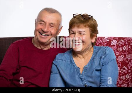 Ein älteres lächelndes Ehepaar schaute auf die Kamera und saß zu Hause auf der Couch. Stockfoto
