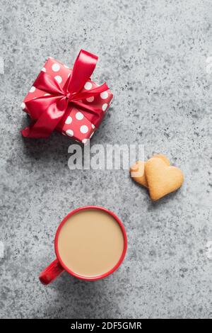 Kaffeetasse und Geschenk, hausgemachte Herzkeks auf grauem Tisch. Grußkarte zum Valentinstag. Draufsicht. Vertikales Format. Stockfoto