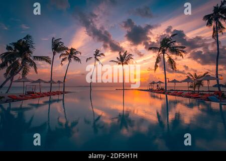 Wunderschöner Pool und Sonnenuntergang. Luxuriöse tropische Strandlandschaft, Liegestühle und Liegen und Wasserspiegelung. Luxus Sommer entspannen, Chill Vibes Stockfoto