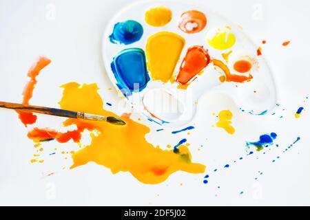 Farbtropfen haben sich auf einem weißen Hintergrund ausgebreitet, daneben liegen eine bunte Palette und ein Pinsel. Kreativer Prozess. Kreative Unordnung. Art. Stockfoto